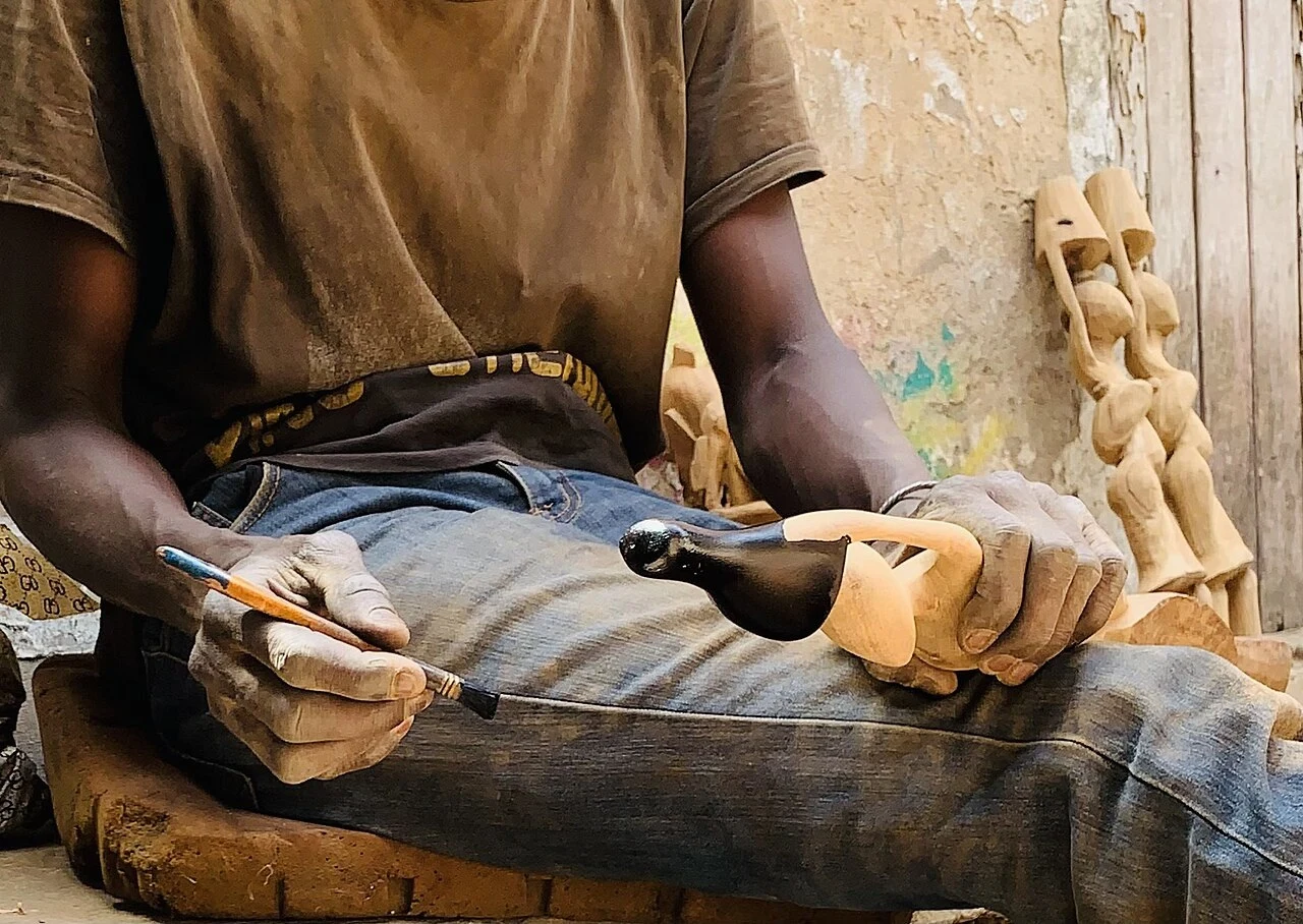 Artisan sculptant le bois à Guédiawaye. Photo d’illustration du savoir-faire local ; elle ne montre pas la fabrication des podiums des JOJ.